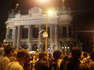 Manifestante sobre poste diante do municipal exibindo seu cartaz.