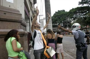 manifestante de braços levantados sendo atacado com spray de pimenta por policial.