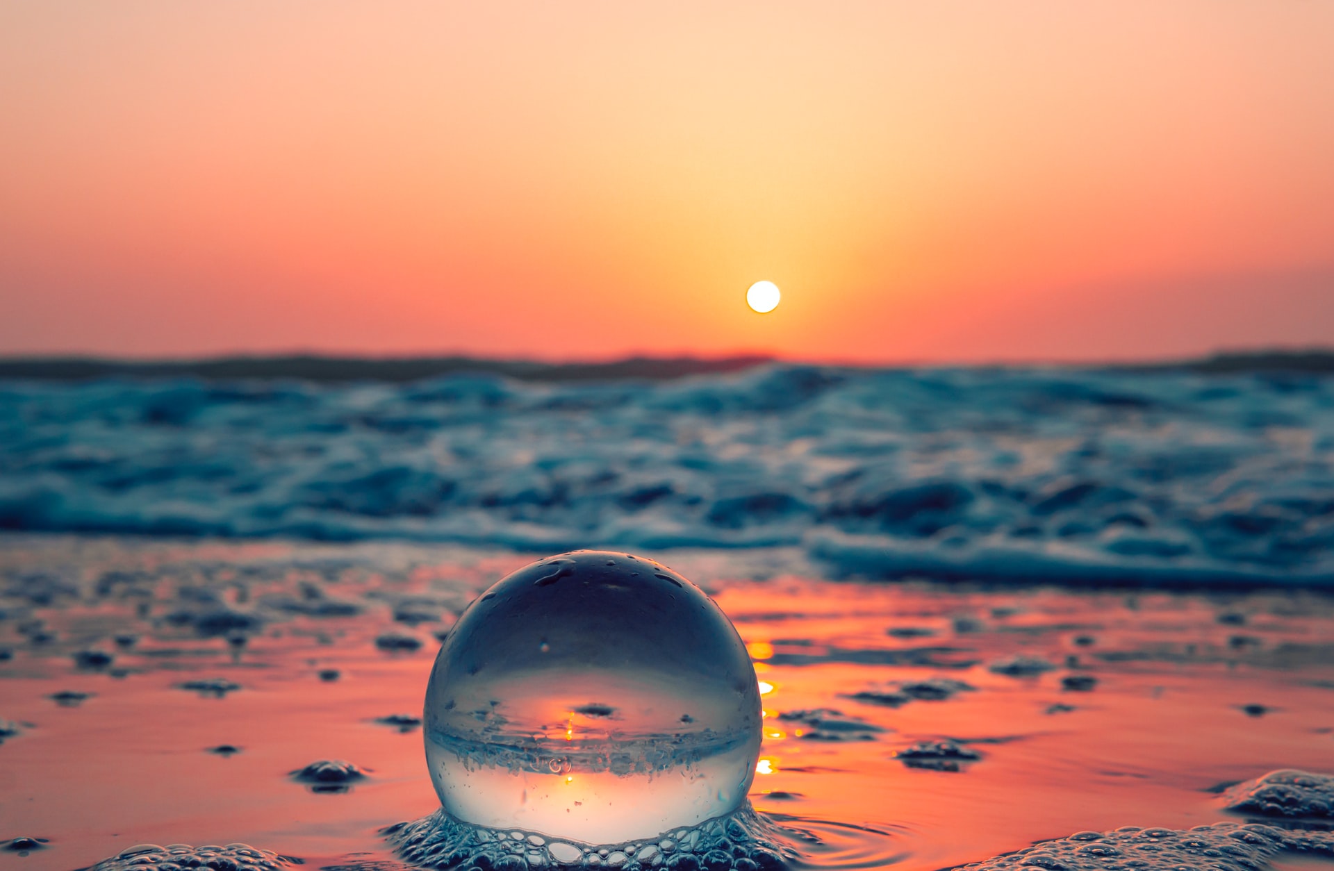 Imagem de uma esfera de vidro refletindo o mar e o Sol